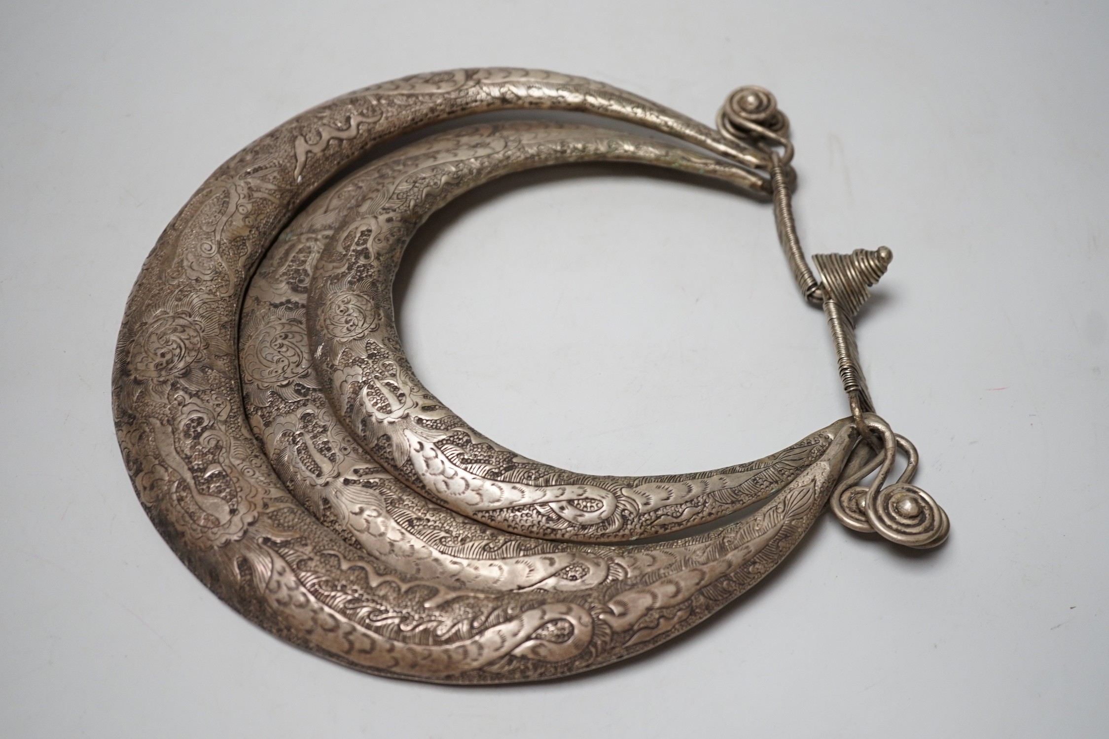 A Chinese Miao white metal triple necklace, repousse worked with dragons and twin fish, 25cm wide